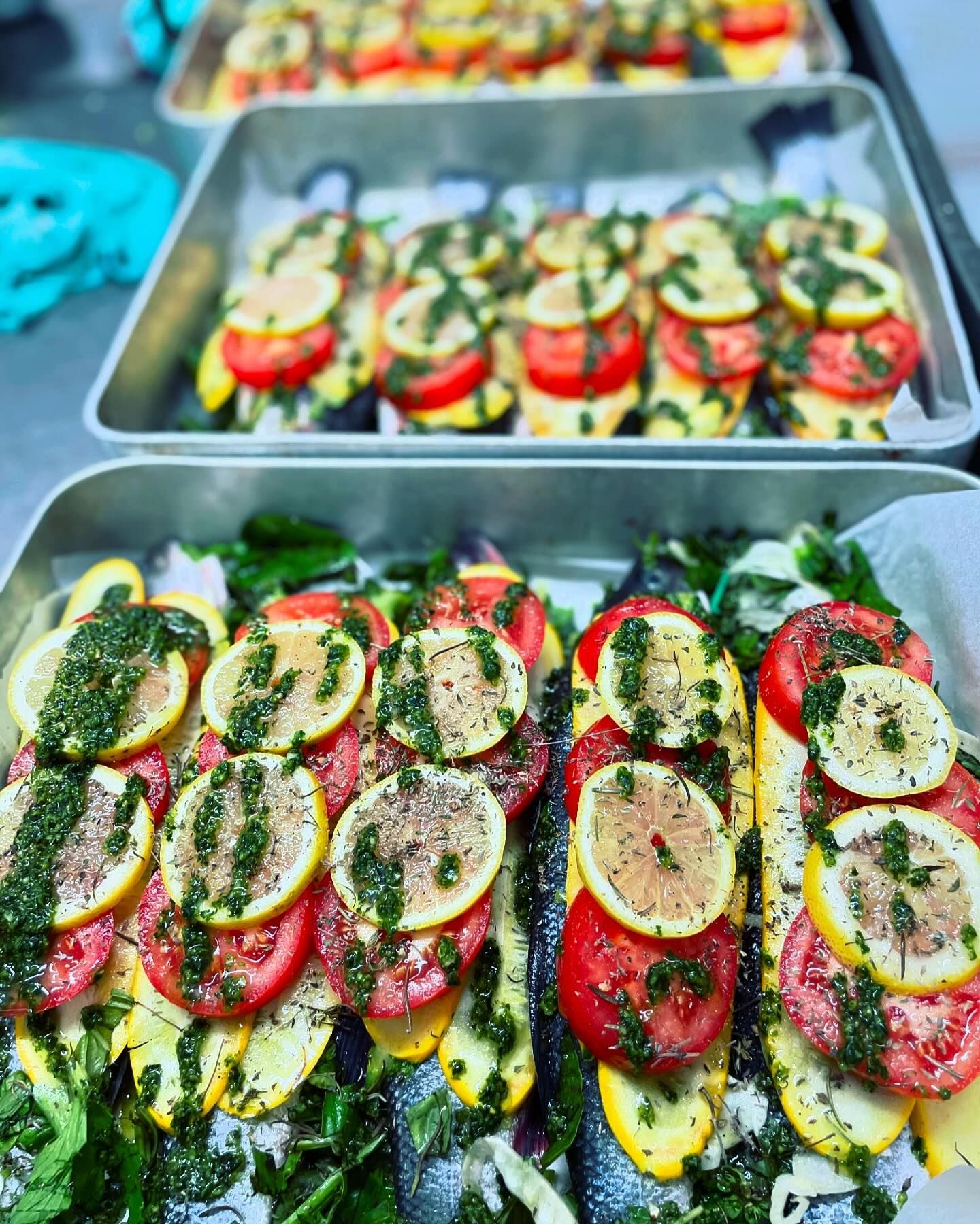 Des poissons préparés dans des plats, recouverts de tranches de tomate, de citron, de courgette jaune et d'huile aux herbes